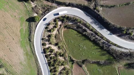 Top-down-aerial-shot-of-a-hairpin-bend-on-a-European-road-with-cars-driving