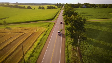 aerial of cars driving down a road in a picturesque countryside on an idyllic august morning