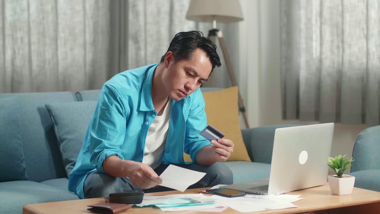 Pria Asia dengan Laptop Melihat Tagihan dan Kartu Kredit, Menggelengkan Kepala Lalu Pusing