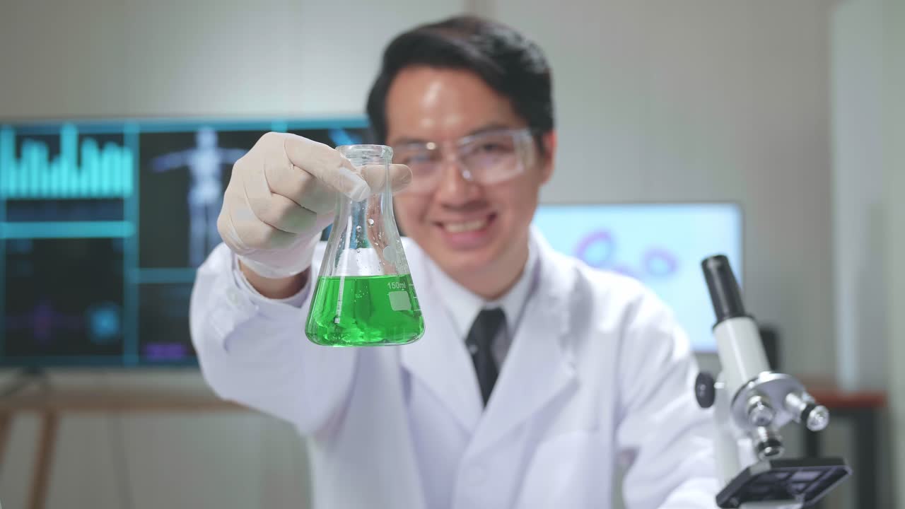 Young Asian Male Research Scientist Looking  Glass Test Tube And Warmly Smiles Into The Camera