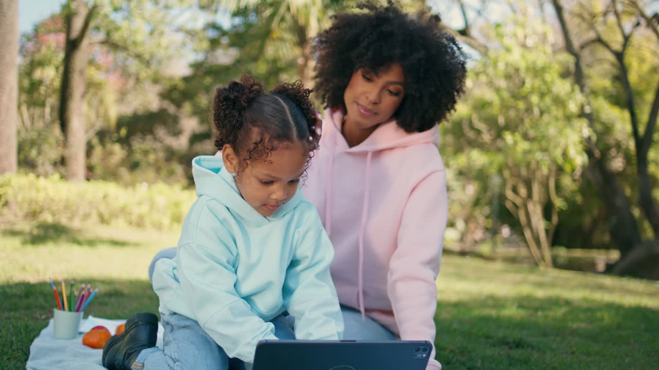Family relaxing tablet in green park close up. Daughter focused on tab