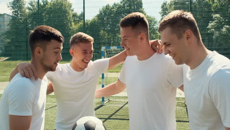 happy young street soccer players with ball standing in circle and embracing on the pitch before football game