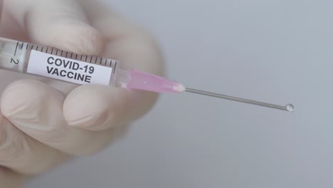 fluid drops ejected from a syringe through hypodermic needle - covid-19 vaccine - close up