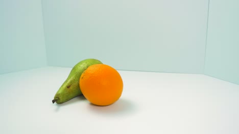 fresh big green pear, juicy orange rotates slowly on a light blue background, healthy food concept, close up shot, camera rotate right