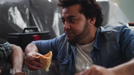 bearded afro-american man talks to colleague eating pizza