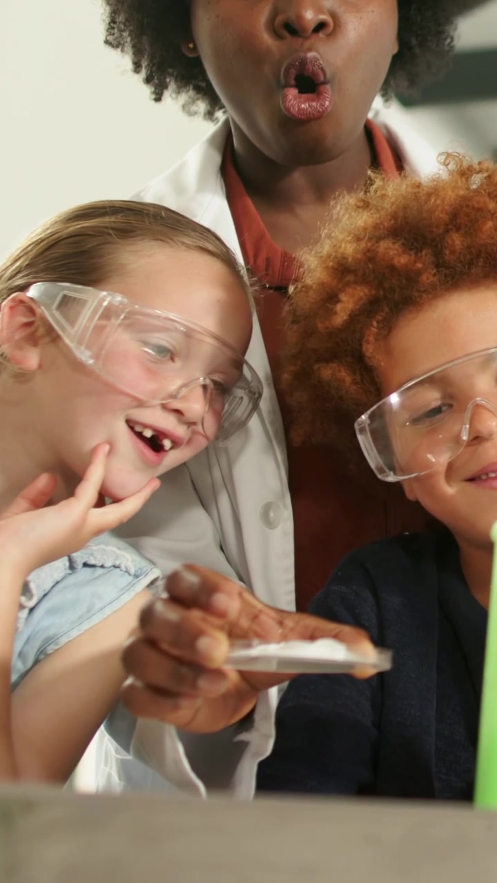 Vertical video: Placing dish, teacher in lab coat guiding goggled kids pinching white gel for demo