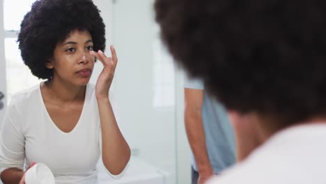 Mujer-Afroamericana-Aplicando-Crema-Facial-Mientras-Se-Mira-En-El-Espejo-En-Casa