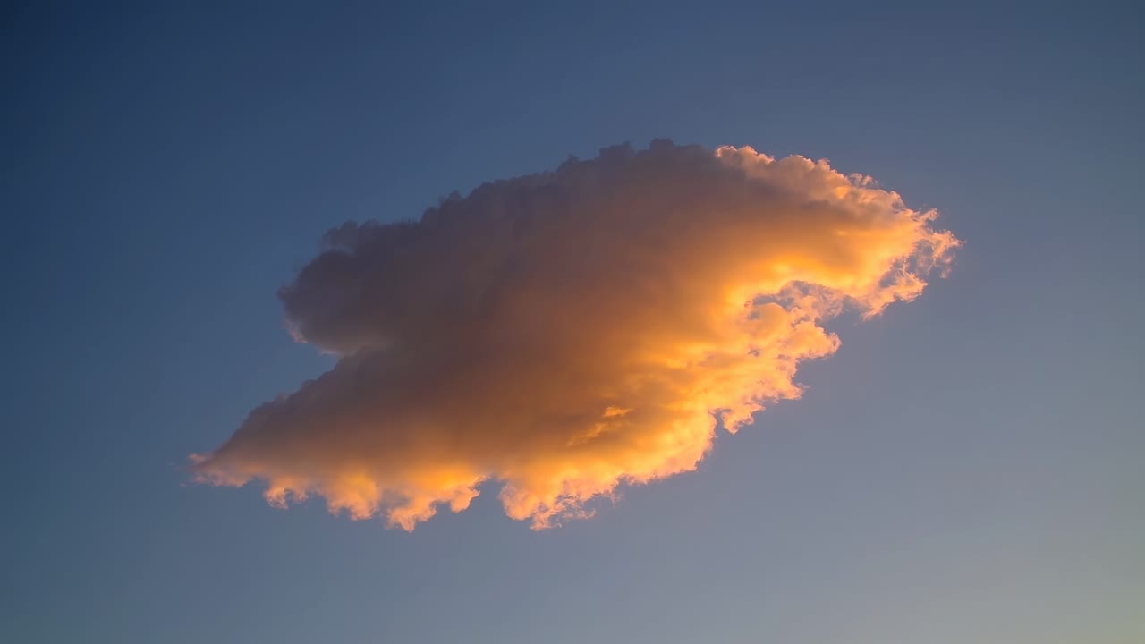 A stunning low-angle shot of a single cloud illuminated by sunset hues against a clear sky, perfect