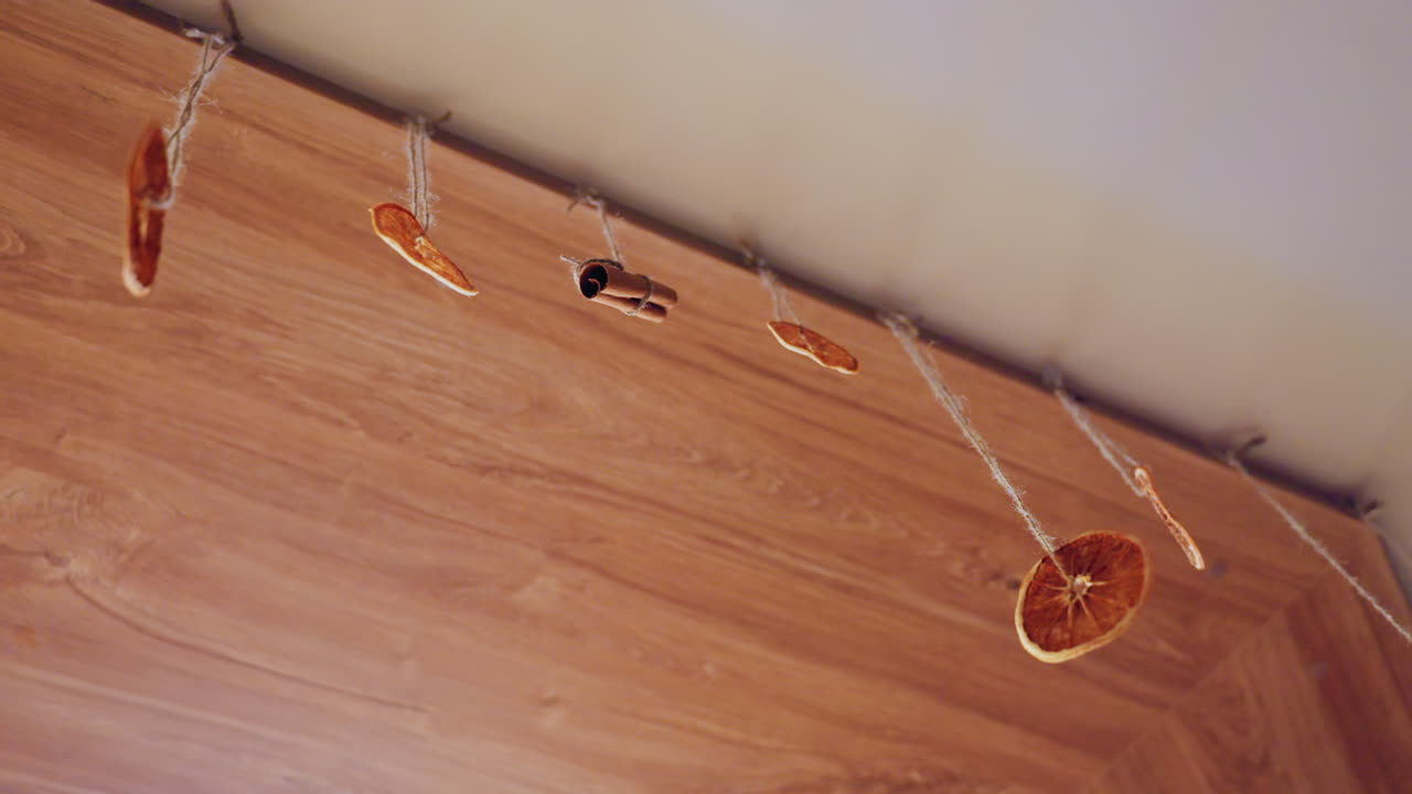 Ghirlanda di fette d'arancia essiccate appesa sopra un angolo di legno con clip per luci a stringa, decorazione boho rustica per un accogliente raccolto autunnale, calde tonalità ambra, pavimento in legno texturizzato, artigianato fai-da-te fatto a mano, primo piano.