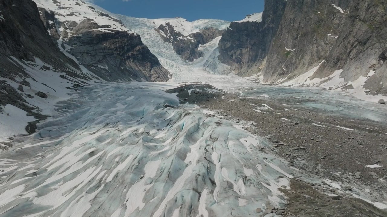 Drohnen-Luftaufnahmen über dem Austerdalsbreen Gletscher in Norwegen, die beeindruckende Eisformationen, gefrorene Strukturen, tiefe Gletscherspalten und abstrakte Gletschermuster unter blauem Himmel präsentieren.