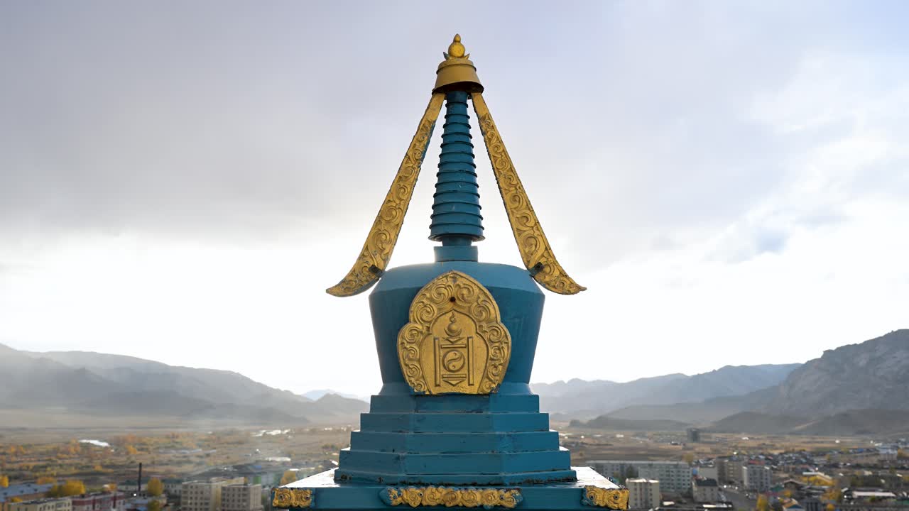 A close-up of a sacred Buddhist stupa with ornate golden details and the Mongolian Soyombo symbol. This religious monument overlooks the town of Uliastai and a remote mountain valley