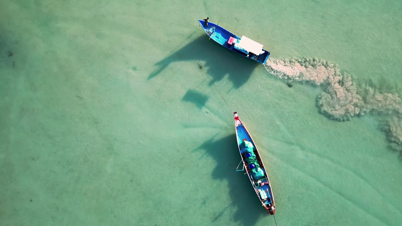 Aerial view of boats floating over turquoise waters in Koh Phangan, Thailand, with scattered debris floating near the shoreline as boat pollutes in sandy waters