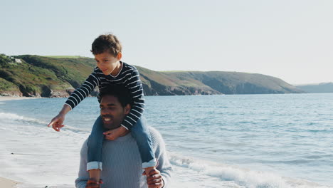 loving father giving son piggyback as they walk along beach together