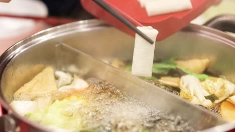 a close-up view of a hotpot with bubbling broth, tofu, mushrooms, and leafy greens being prepared.