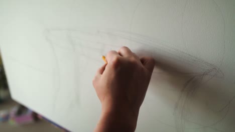 mujer de diseño joven de cabello largo en delantal beige dibujando boceto en lienzo usando lápiz gris en un estudio de taller, lugar artístico. primer plano de dibujo en lienzo