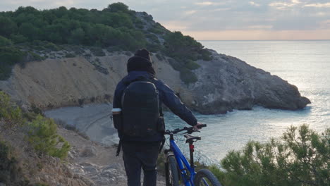 traveller pushing bike along the cliff walk with a stunning beach view in early morning light