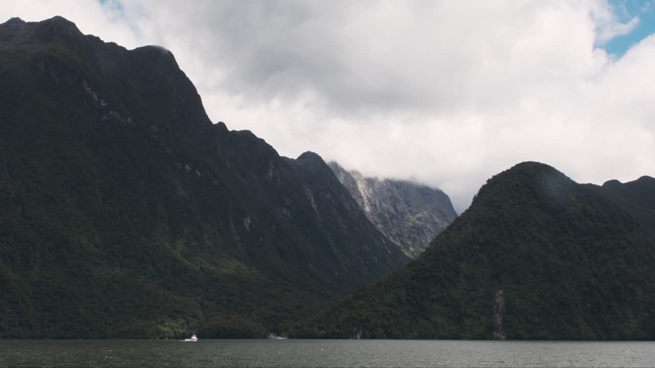 Boat appears minuscule as it travels next to the immense cliffs of Milford Sound