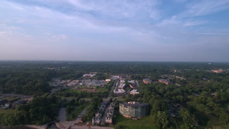 Lake-Erie-beach-front-drone-over-water-facing-south,-reverse-dolly,-showing-green-trees,-residential-neighborhoods-and-office-buildings