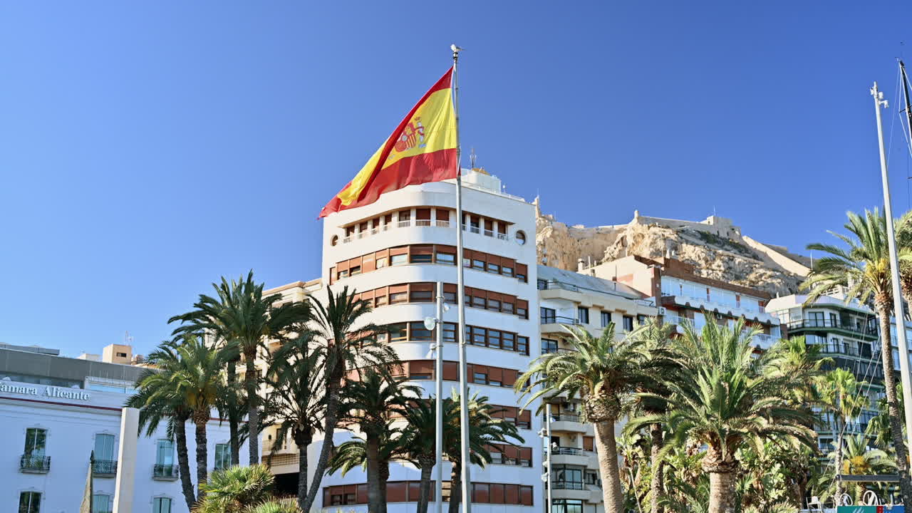 Spansk flag, der vinker i Alicante, Spanien. Santa Barbara-slottet på bjerget Benacantil i baggrunden