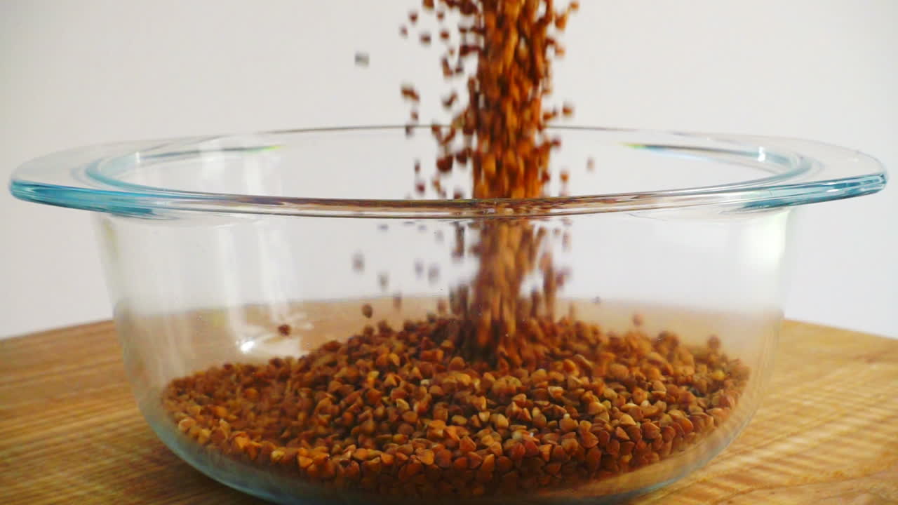 Buckwheat is poured into a glass pan. Slow Motion