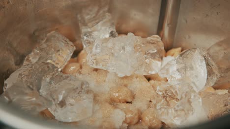 Dropping-ice-cubes-in-a-bowl-with-chickpeas,-close-up