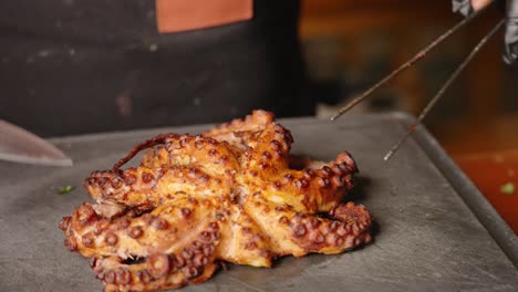 male chef presenting a perfectly cooked and tenderized octopus with golden brown crisp surface by rotating it on chopping board, before it is cut and slice, slow motion shot