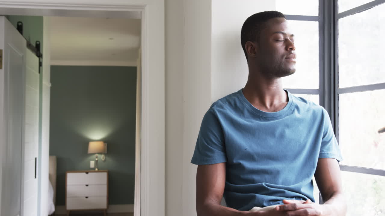 Relaxing by window, young man enjoying peaceful moment at home, copy space