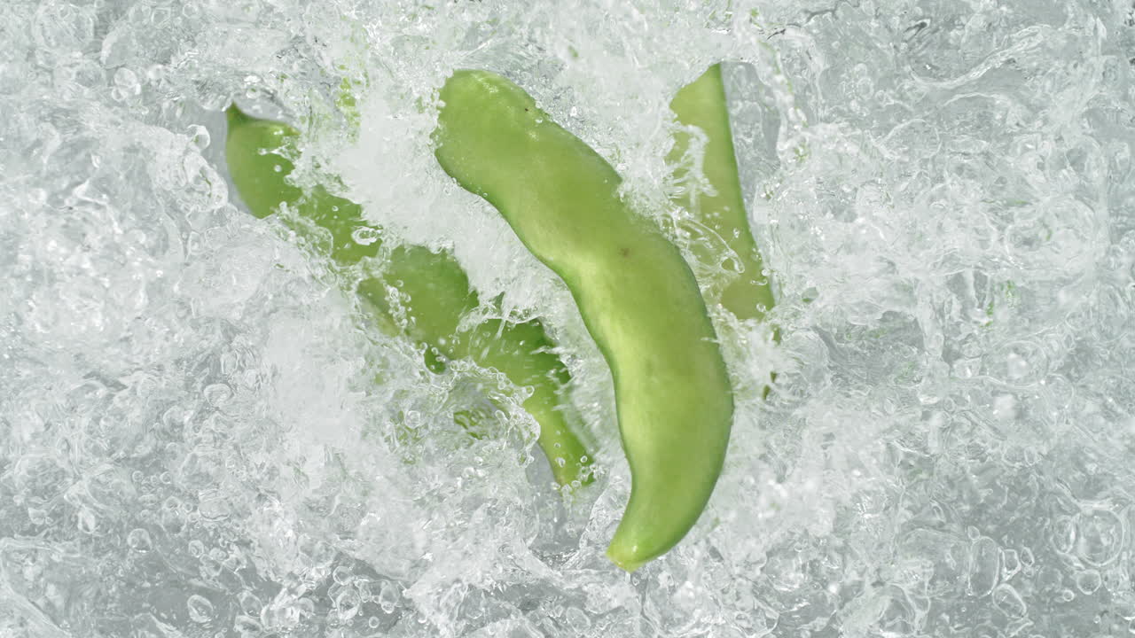 Broad Bean Pods Falling Into Pot Of Boiling Water Making A Splash In Slow Motion, Table Top View