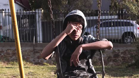 a teenage boy sits on a park swing