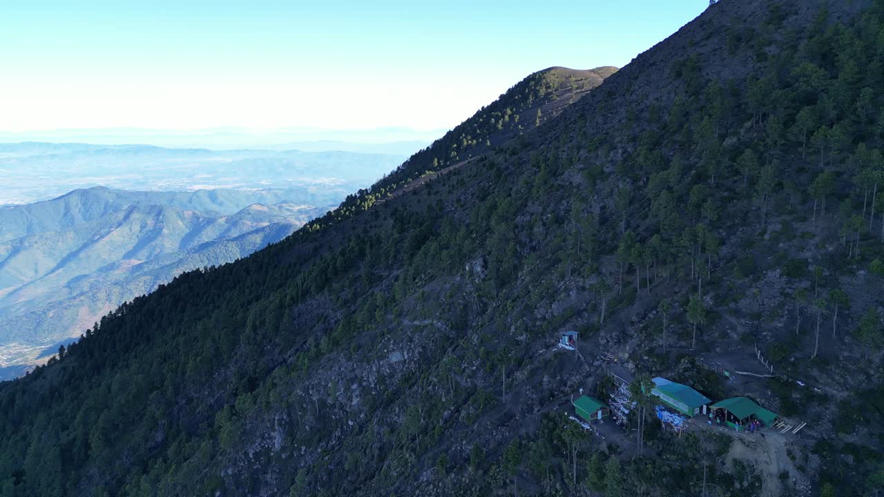 vista de drones en guatemala volando sobre una montaña volcánica cubierta de árboles verdes y un campamento en una colina