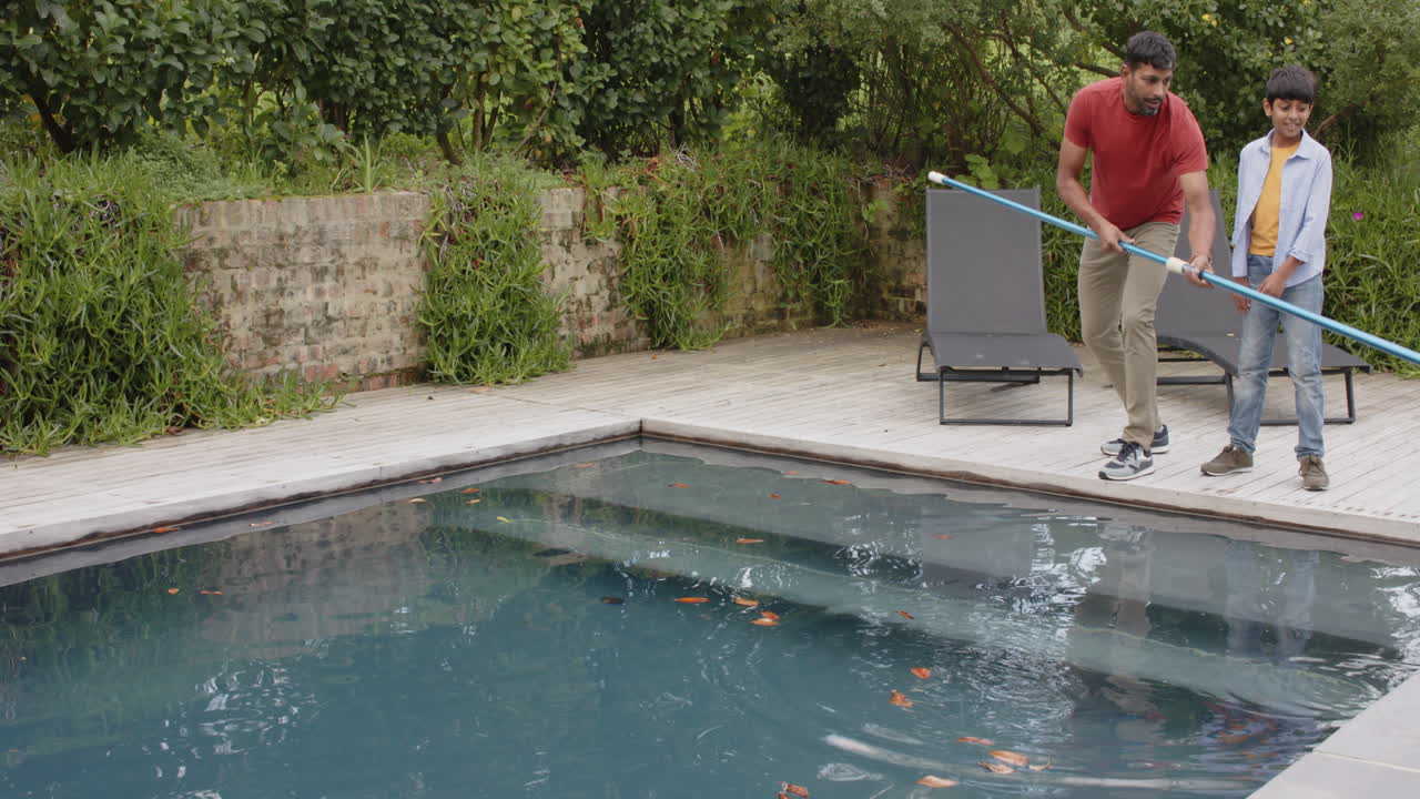 Cleaning swimming pool, Indian father and son working together outdoors in backyard, copy space