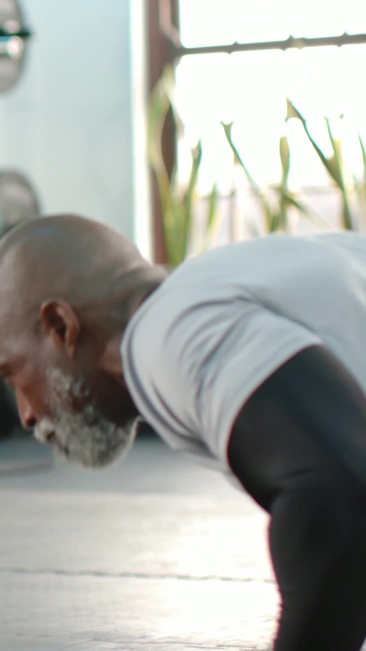 Vertical video: Doing pushups man in gray tee lowering on mat, coach coming touching guiding