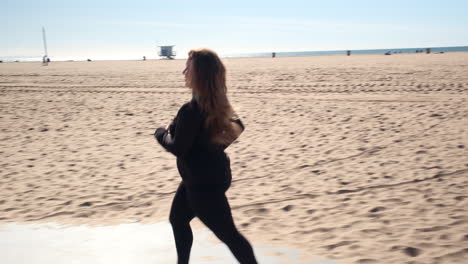 Confident-independent-jogger-woman-running-on-the-beach-of-Santa-Monica-California,-with-a-fair-in-the-background