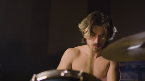 young shirtless male drummer with beard playing drums