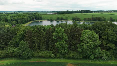 Behind-a-massive-green-wall-out-of-trees-reservoir-Kettering-is-seen-from-above