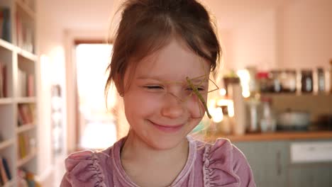 cute kid girl portrait holds stick insect pet in hands and put it on her face at home have fun and smile