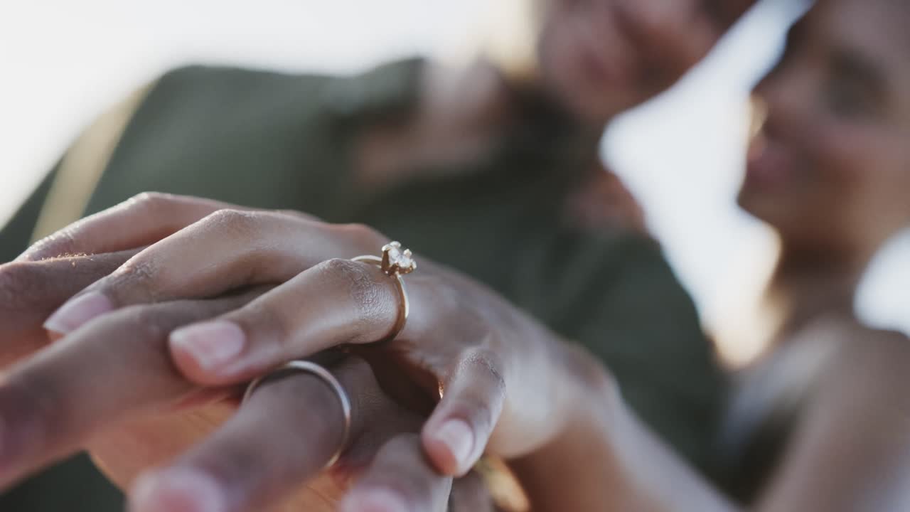 Diverse bride and groom showing wedding rings at beach wedding, selective focus, in slow motion