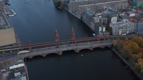 Toma-Aérea-Lenta-Inclinada-Hacia-Abajo-En-El-Famoso-Puente-Oberbaum-En-Berlín,-Alemania-Con-Autobús-Amarillo-Y-Tráfico-De-Automóviles,-Vista-Aérea-De-Drones