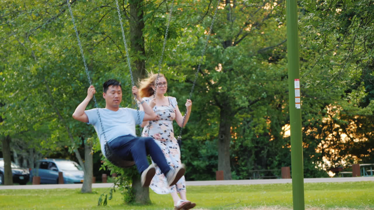 그네를 타고 공원에서 쉬고 있는 활동적인 젊은 가족 임산부와 아시아인