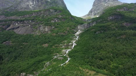 river flowing down hillside in olden norway - tall mountains and lush forest with melted glacier water - norway aerial