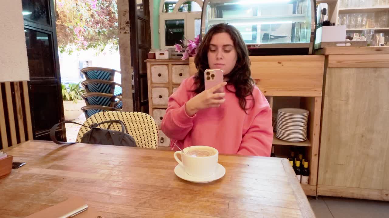 una mujer está sentada en una mesa con un teléfono celular en la mano