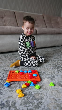 positive smiling caucasian baby plays with bright toy. lovely cute toddler plays on the floor at home. vertical video.