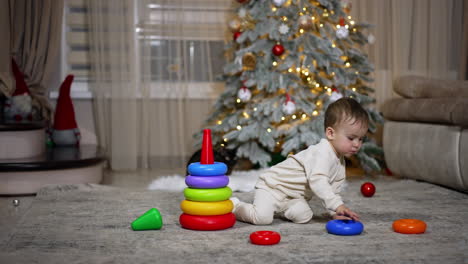 baby playing with stacking rings near christmas tree