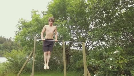 young man exercises by doing muscle-up pullups outdoors on home gym