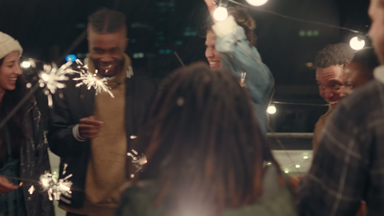 grupo multiétnico de amigos sosteniendo bengalas celebrando la víspera de año nuevo divirtiéndose bailando bajo la lluvia en la azotea por la noche disfrutando de la celebración