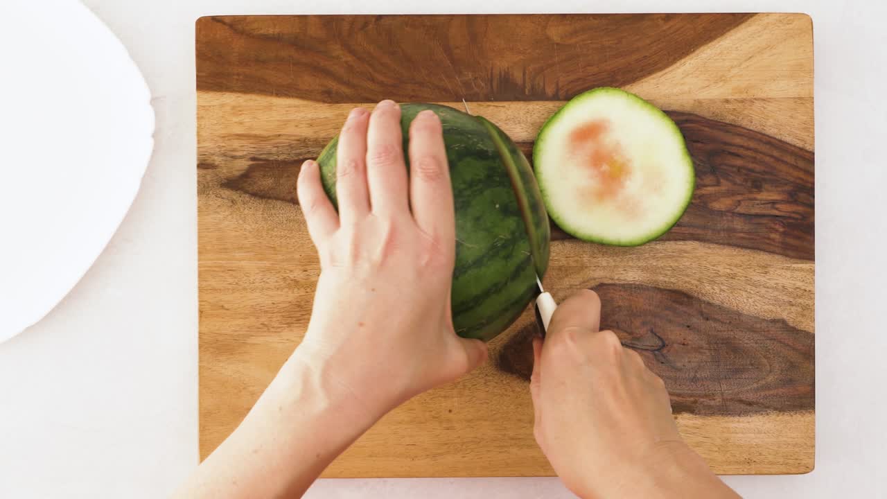 색 배경에 나무로 된 절단판에 수박을 잘라내는 사람. 가까운 가속 비디오, 위에서 볼 수 있습니다.