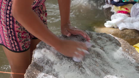 una joven lava ropa en una roca en el río