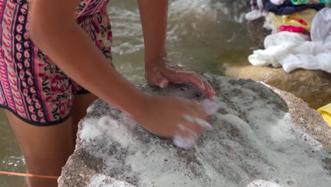 a young woman washes clothes on a rock in the river