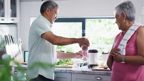 Happy-senior-biracial-couple-preparing-healthy-drink-in-kitchen