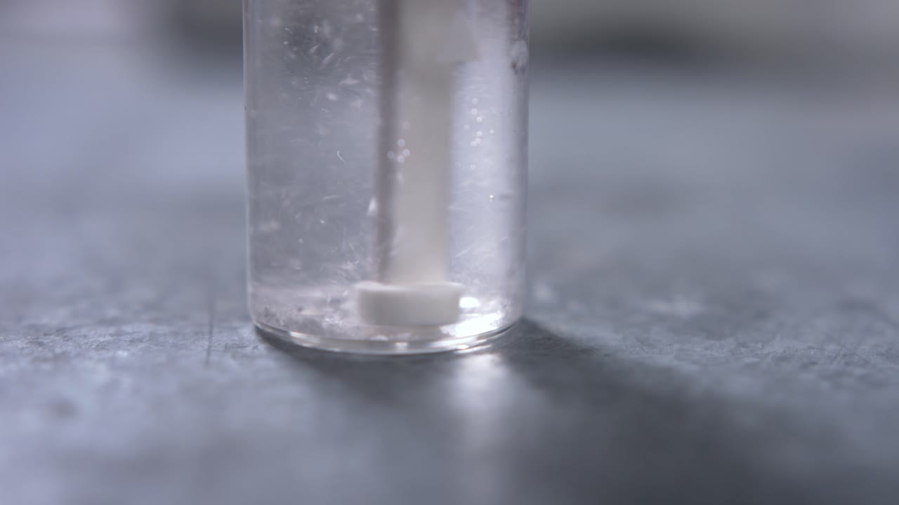 A water treatment tablet is put in the water of a small glass flask and is dissolving after being broken up by a small pestle